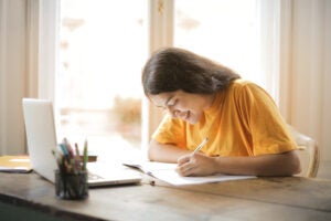 person writing on paper sitting at a desk