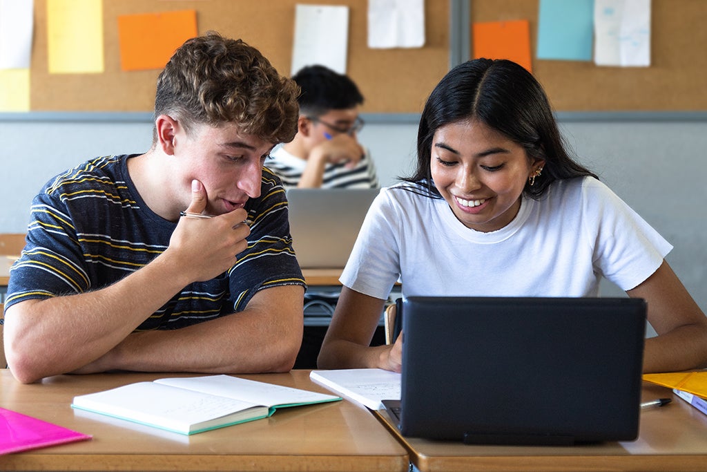 Two high school students in class working together on school project using laptop.