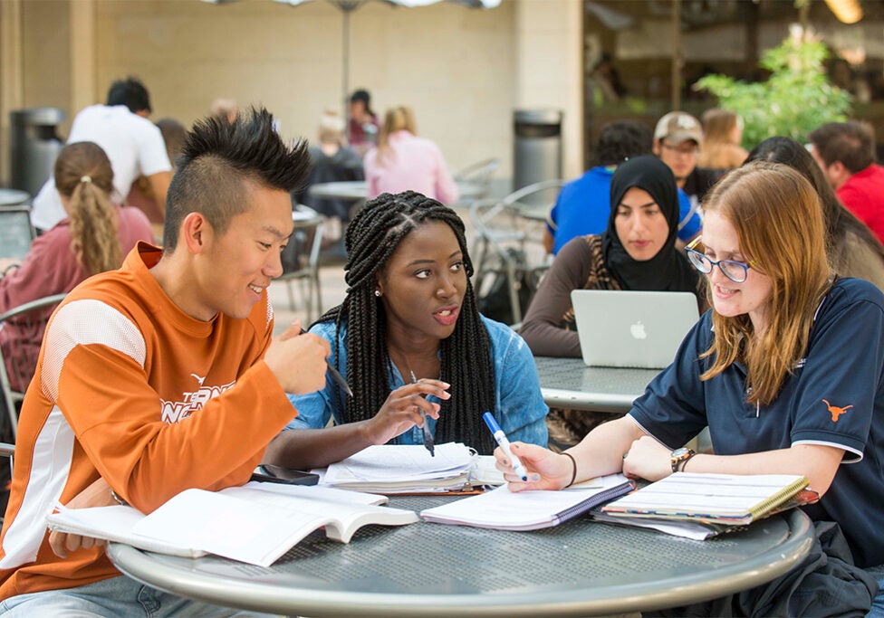 Three students sit around a table working on homework together.