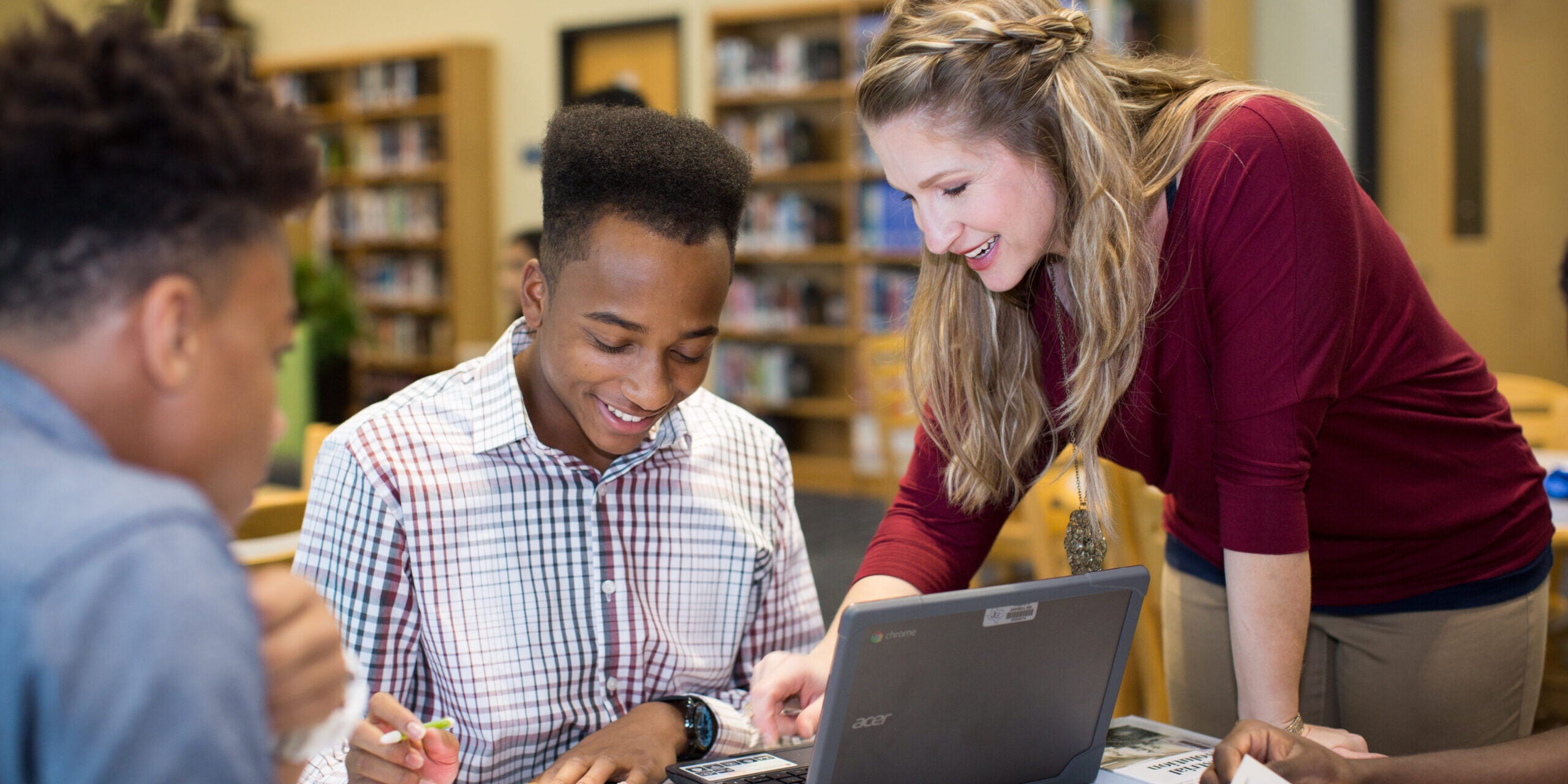 Teacher leans over a desk to help a student with their assignment.