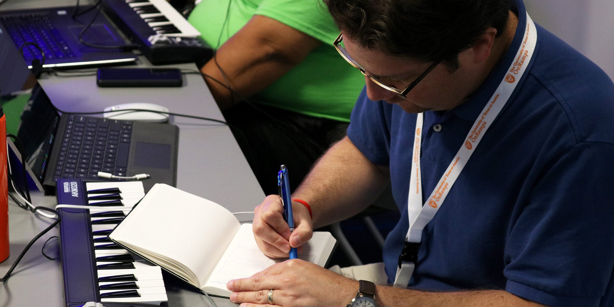 Man writing in a notebook in front of a keyboard